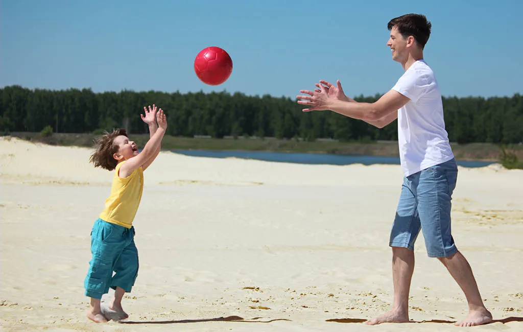 Father and son playing with a ball on the beach.