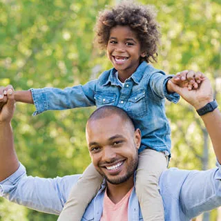 Smiling father carrying his son on his shoulders in the park.