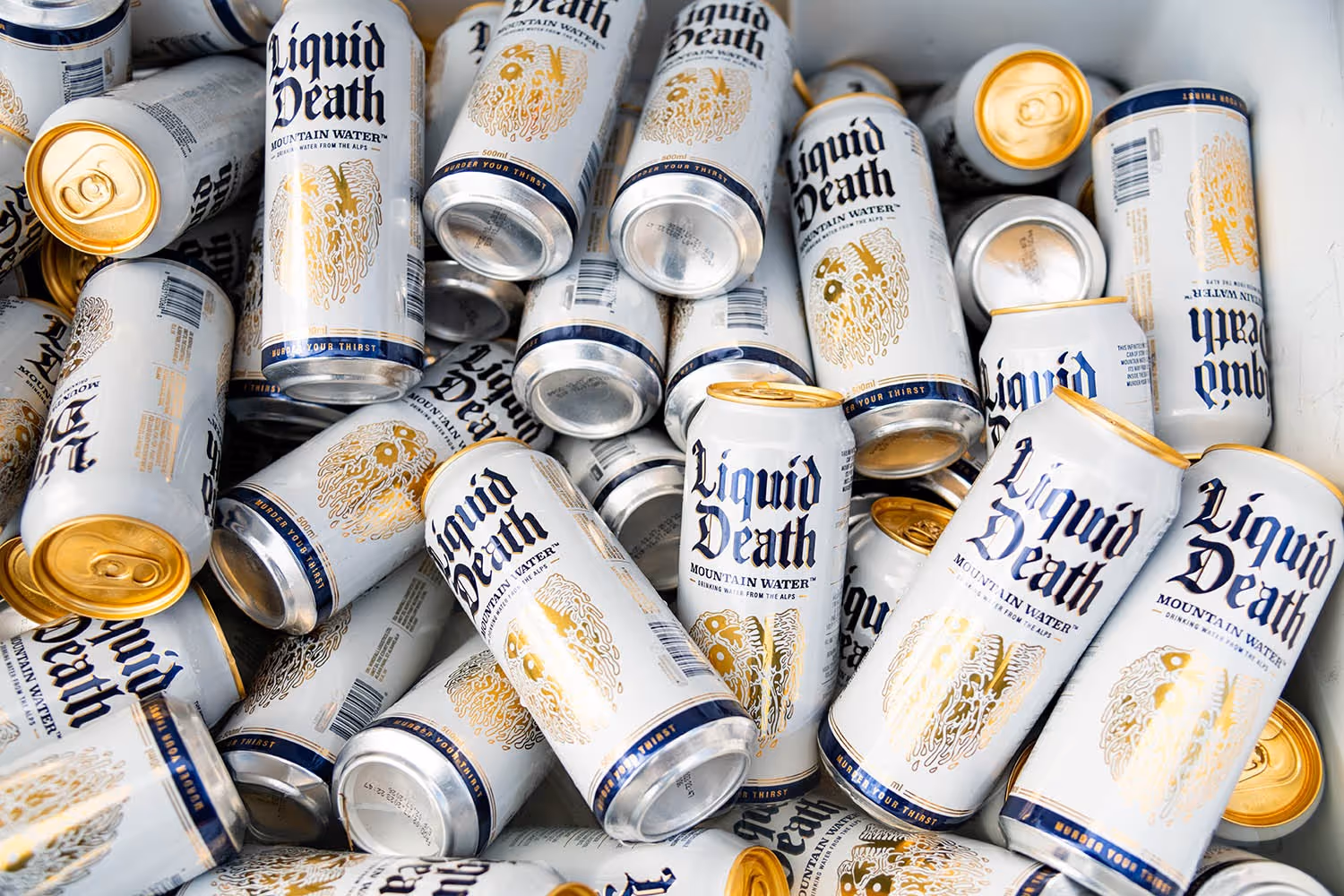 Pile of Liquid Death Mountain Water cans showing the brand's distinctive white-and-gold gothic packaging. The bold, rebellious visual identity is what makes Liquid Death one of the most mentally available beverage brands in its category.