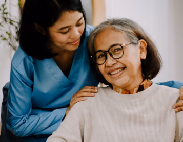 Caregiver rests her hands on the shoulders of a smiling older woman