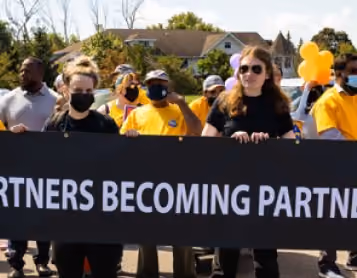 Marchers in yellow shirts carry a Partners Becoming Partners banner at an outdoor rally