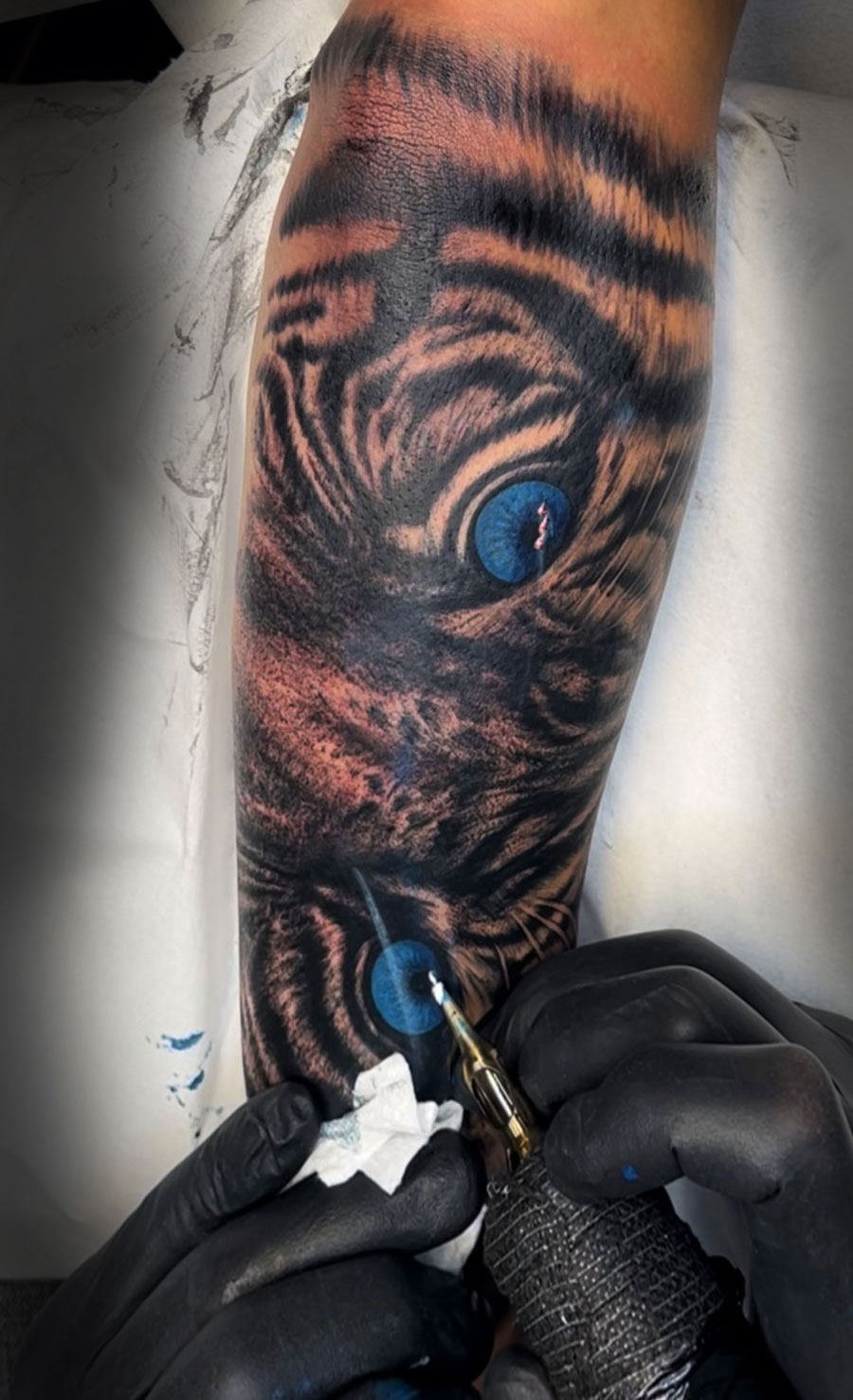 Detailaufnahme beim Tätowieren eines Tigermotivs mit blauen Augen.