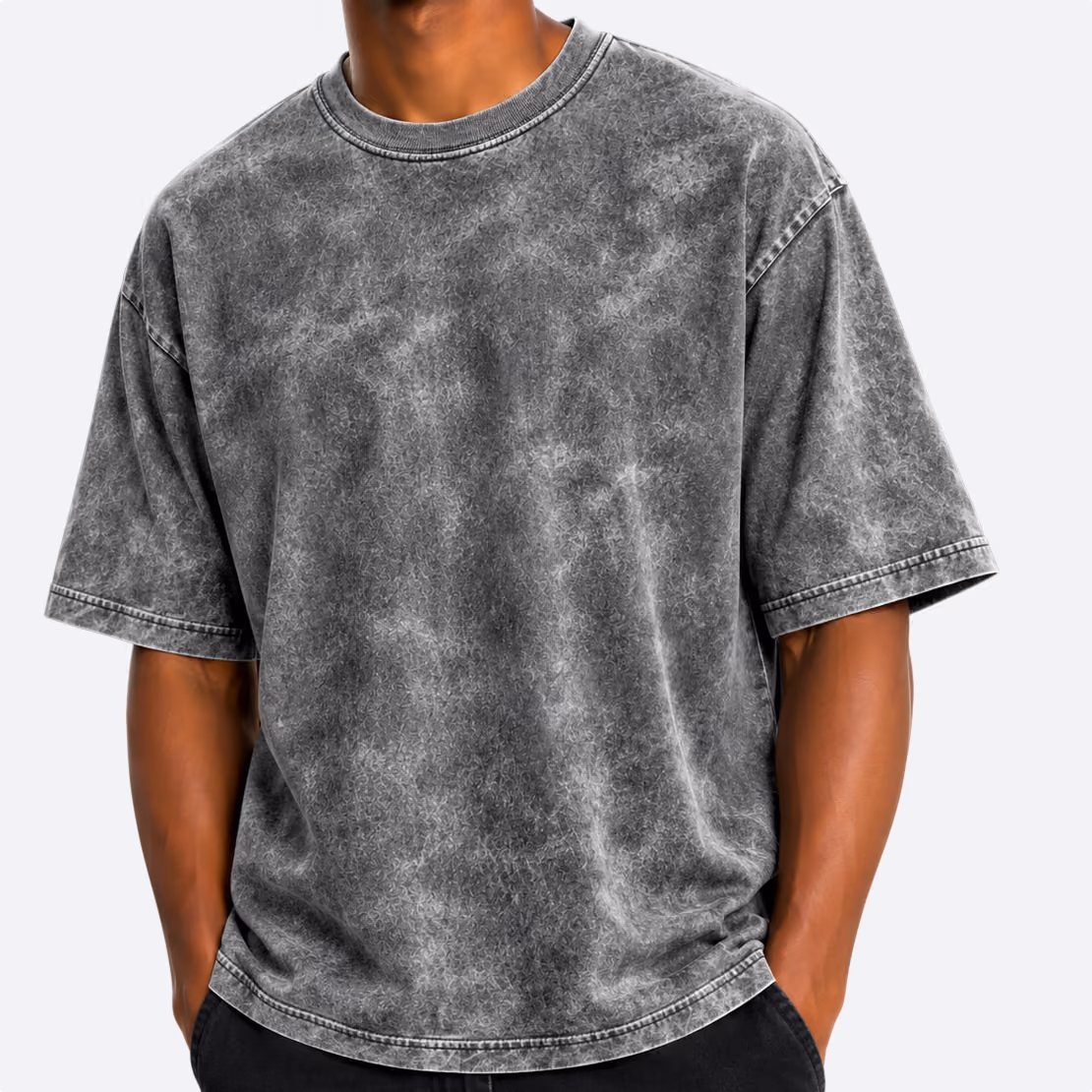 Person wearing a loose-fitting, short-sleeve, acid wash gray T-shirt with their hands in the pockets of black pants.