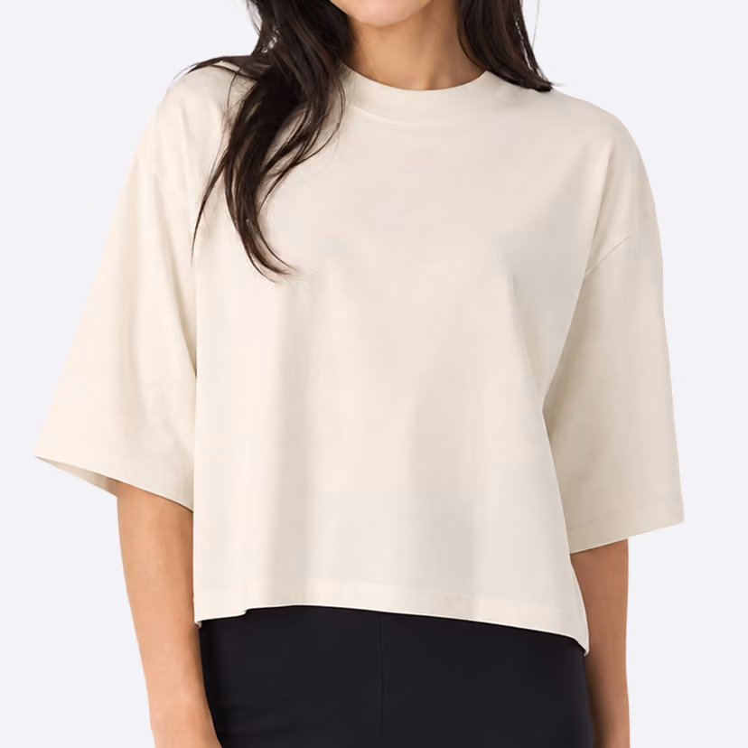 Woman wearing a loose-fitting, beige, short-sleeve crop top paired with high-waisted black pants.