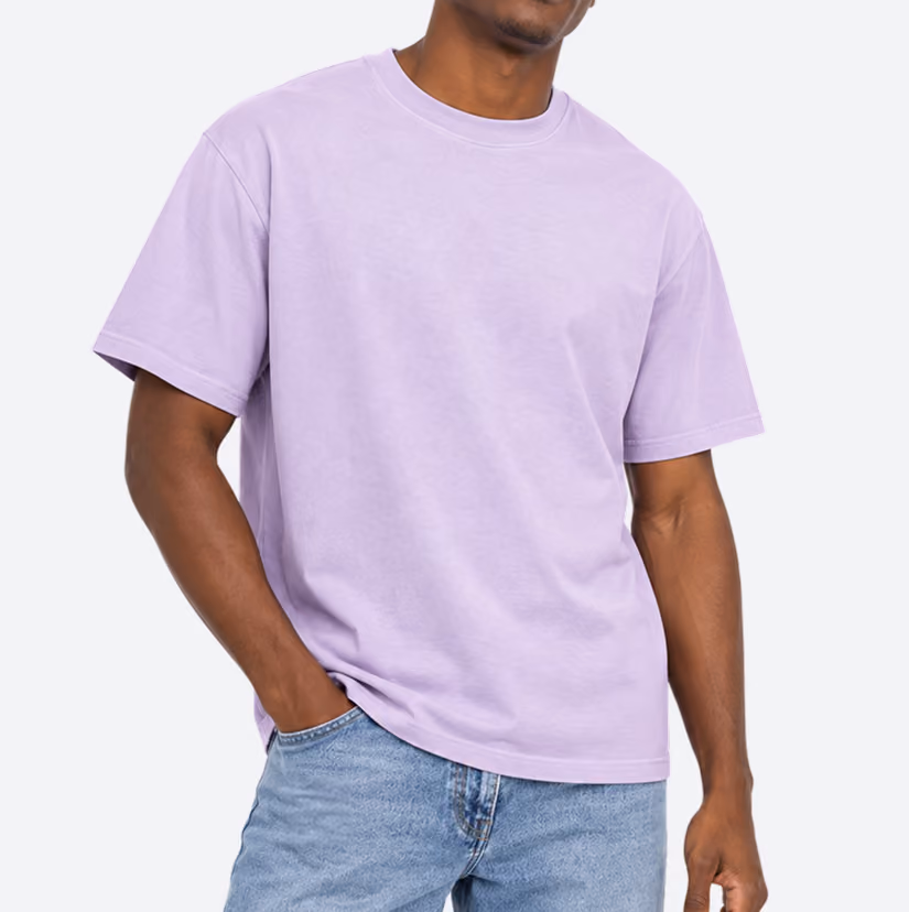 Man wearing a plain lavender short-sleeve t-shirt and light blue jeans with one hand in a pocket.