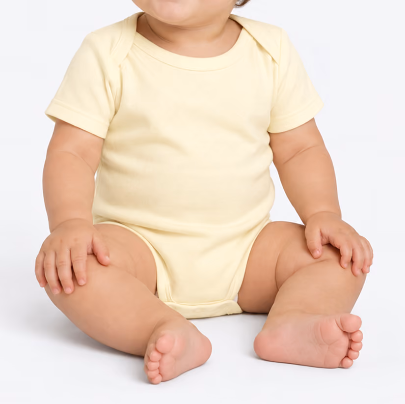 Baby sitting on a white surface wearing a short-sleeve light yellow onesie.