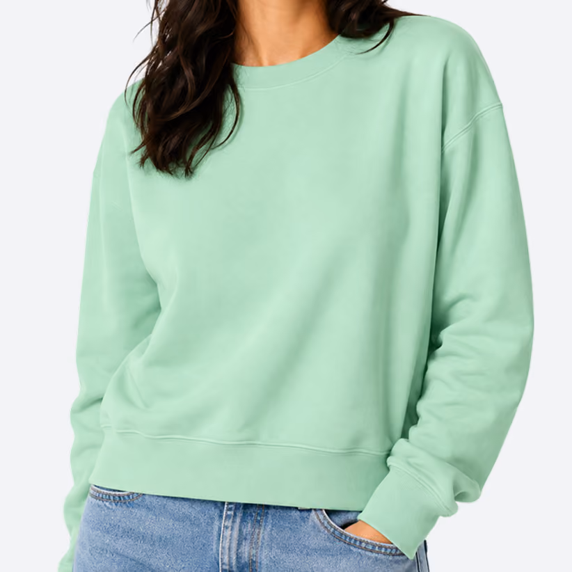 Woman wearing a plain light green sweatshirt with long sleeves and ribbed cuffs, paired with blue denim jeans.