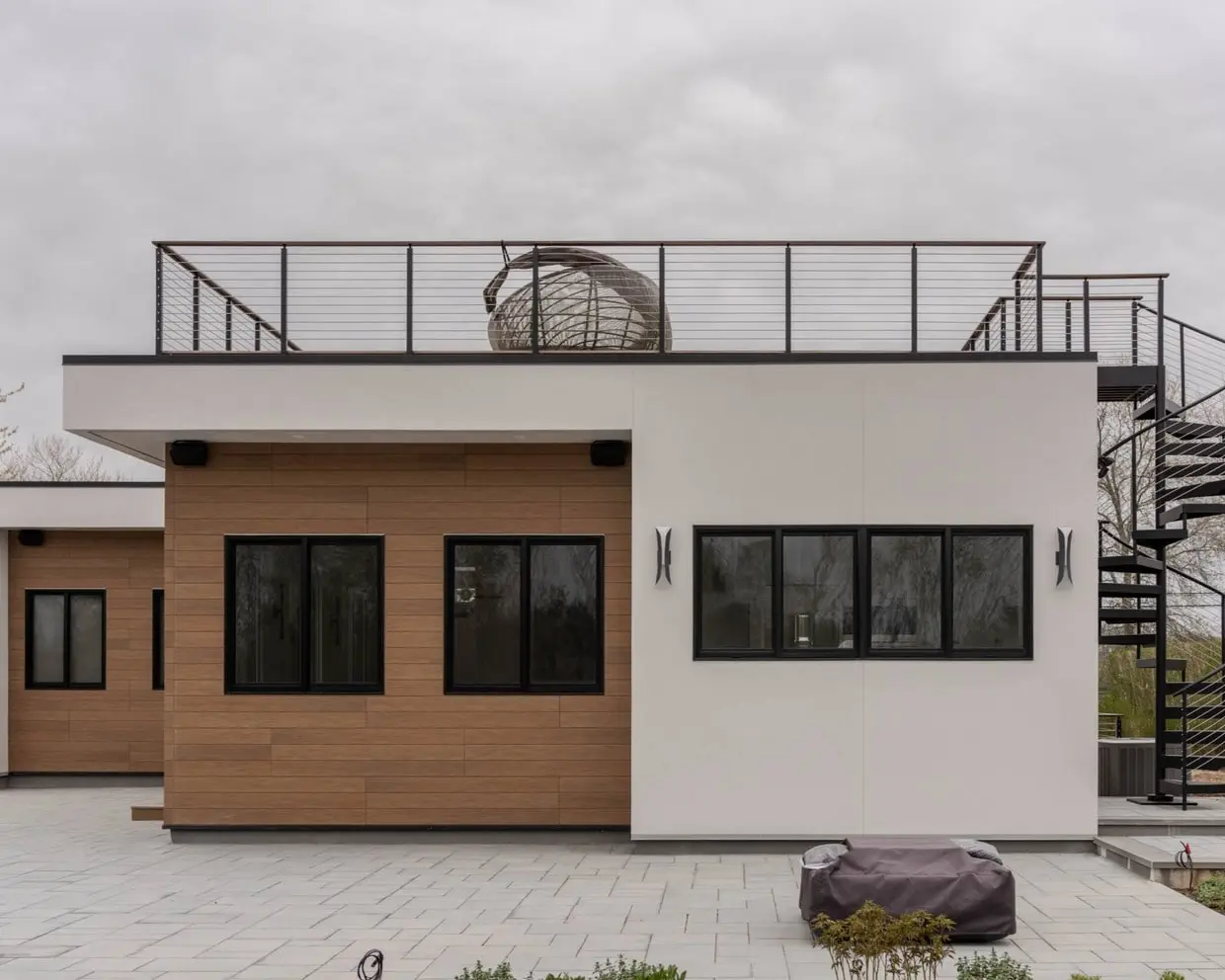 Contemporary home exterior featuring wood siding, black-framed windows, and a rooftop deck with a spiral staircase.