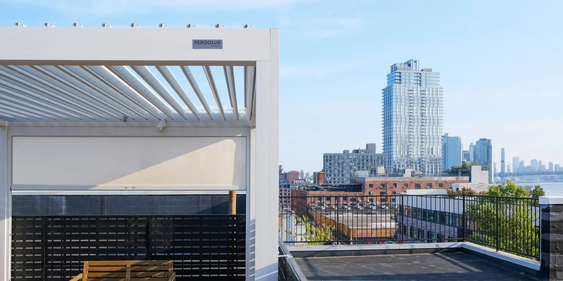 Aerial view of a Greenpoint rooftop deck featuring a louvered pergola, outdoor kitchen, privacy screens, and composite deck tiles.