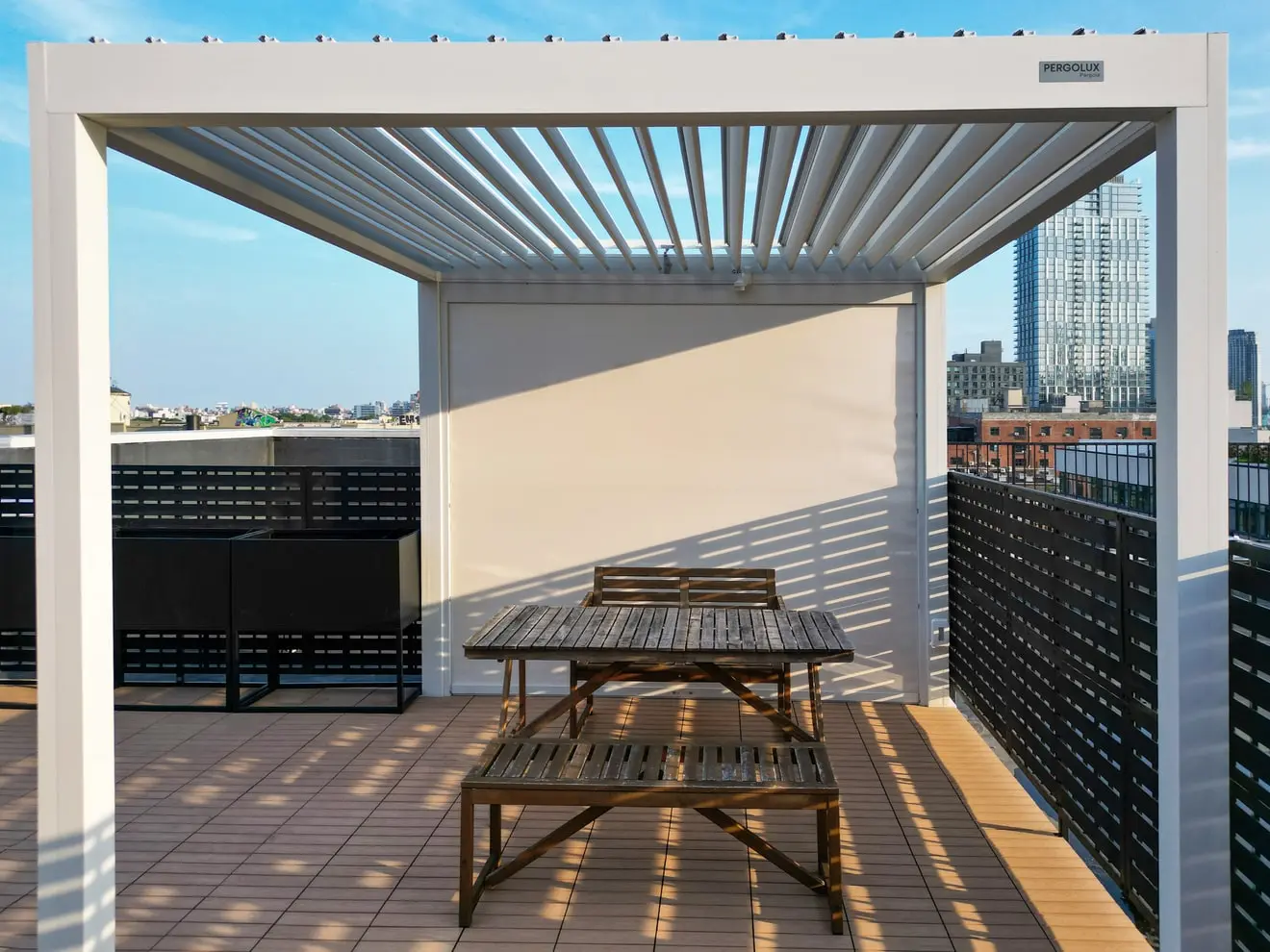Dining area beneath a PERGOLUX louvered pergola on a Greenpoint rooftop deck with composite tiles and privacy screens.