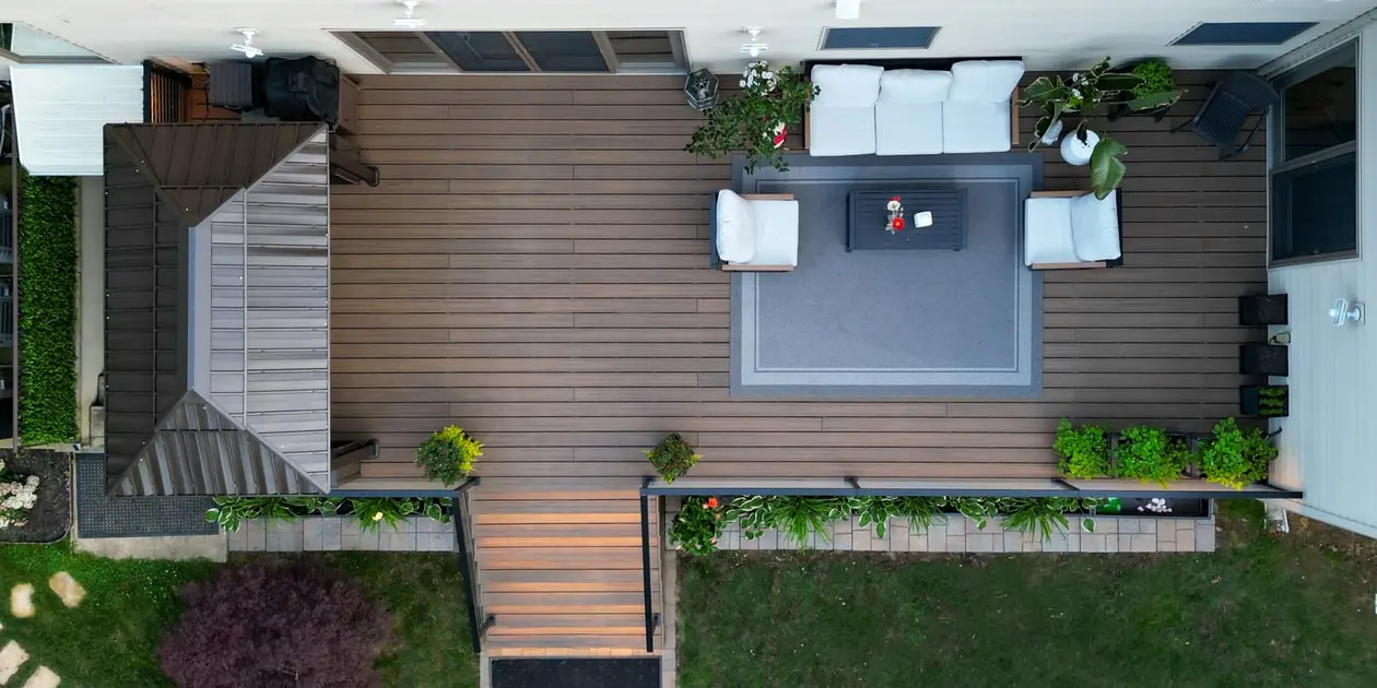 Aerial view of a modern backyard deck with composite decking, built-in seating area, planters, and illuminated steps.