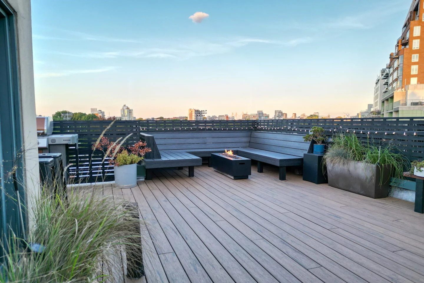 Brooklyn rooftop deck with composite decking, built-in seating, privacy fencing, and fire pit, designed and installed by a rooftop deck builder in NYC.