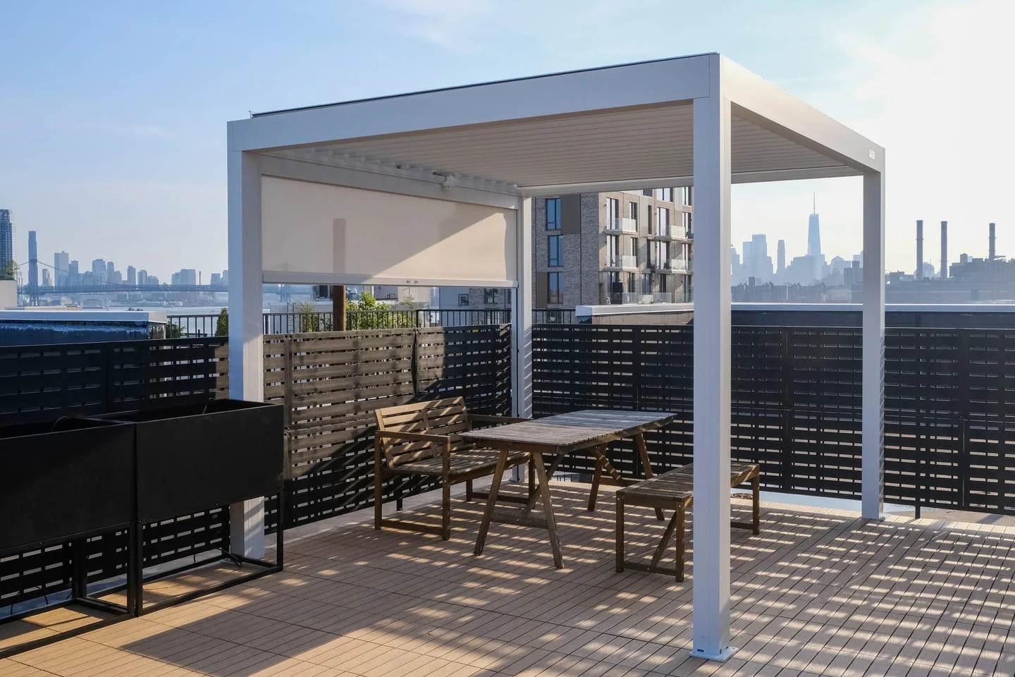 NYC rooftop deck featuring aluminum pergola, composite decking, and horizontal privacy fencing with skyline views.