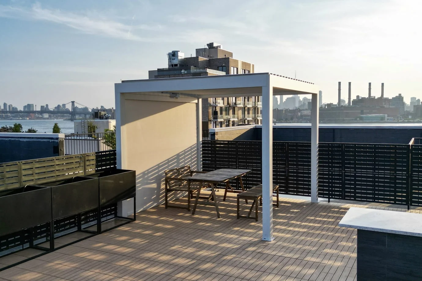 Rooftop deck with composite tile decking, modern white pergola, and black privacy screens with East River and bridge views