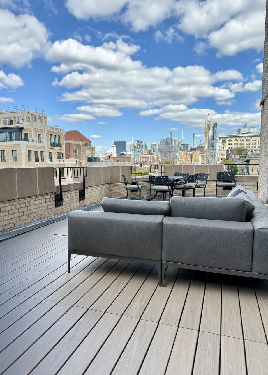 High-rise Manhattan rooftop deck with light gray composite decking, modern sectional sofa, and dining set with Empire State Building and Midtown skyline views