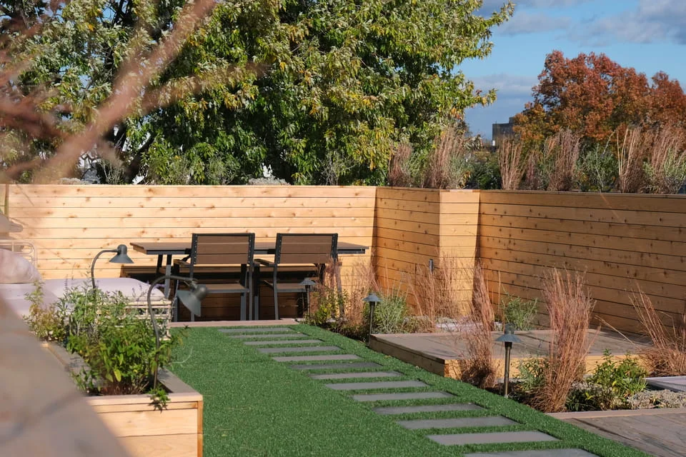 Rooftop dining area with cedar privacy walls, wood decking, planters, and landscape lighting in NYC