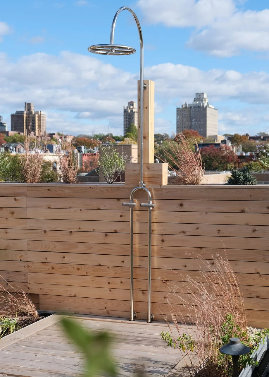 Stainless steel outdoor shower mounted on a cedar privacy wall of a New York rooftop deck