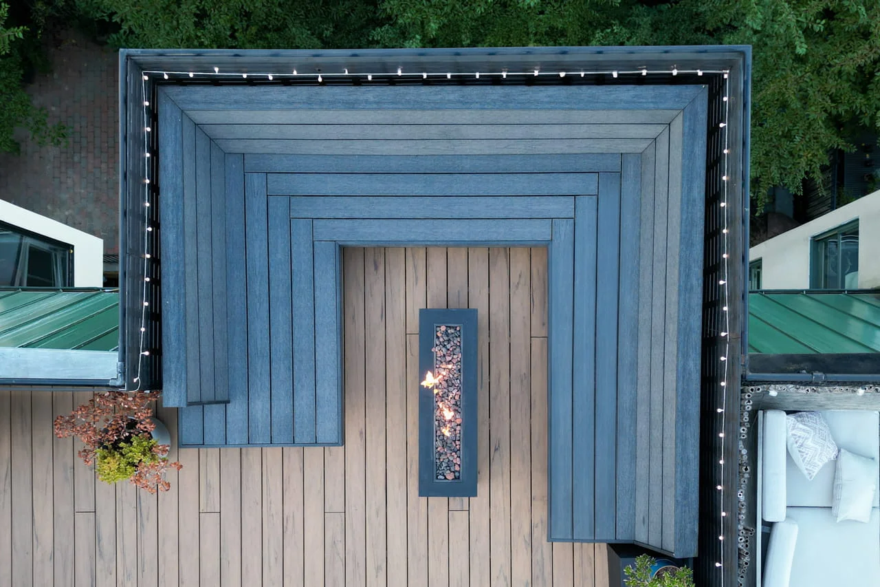 Overhead view of slate-blue composite bench seating wrapped around a linear fire feature on a Brooklyn roof deck