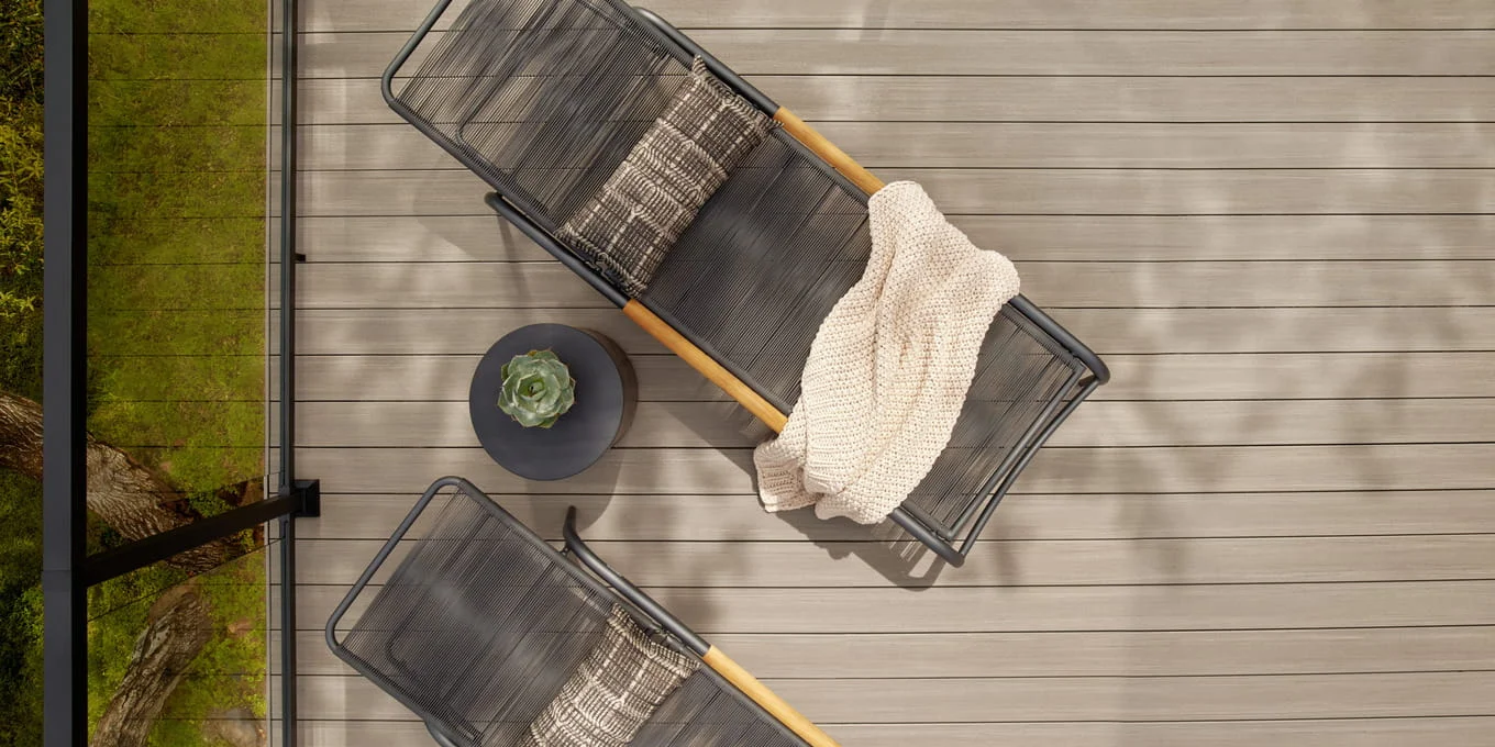 Two black loungers and a side table on light gray composite deck boards, viewed from directly above