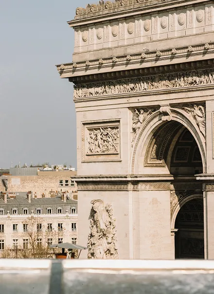 Vue partielle de l'Arc de Triomphe depuis notre hôtel à Paris sous un ciel clair, avec des bâtiments parisiens en arrière-plan.