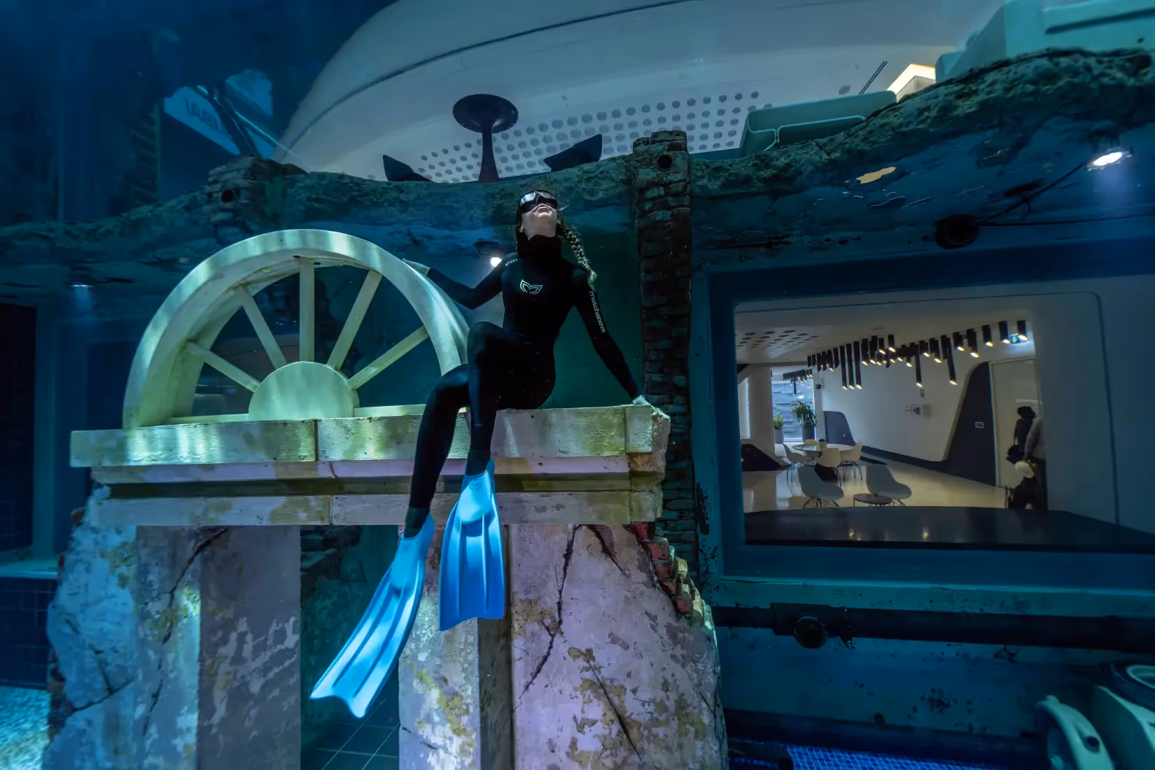 a woman in a black wet suit and fins sitting on a stone ledge