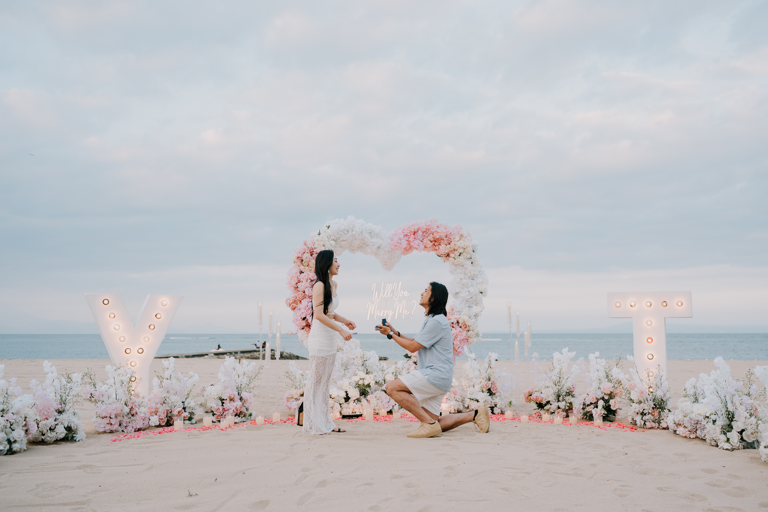 Couple walking towards a cliffside proposal setup with Will You Marry Me written in red rose petals