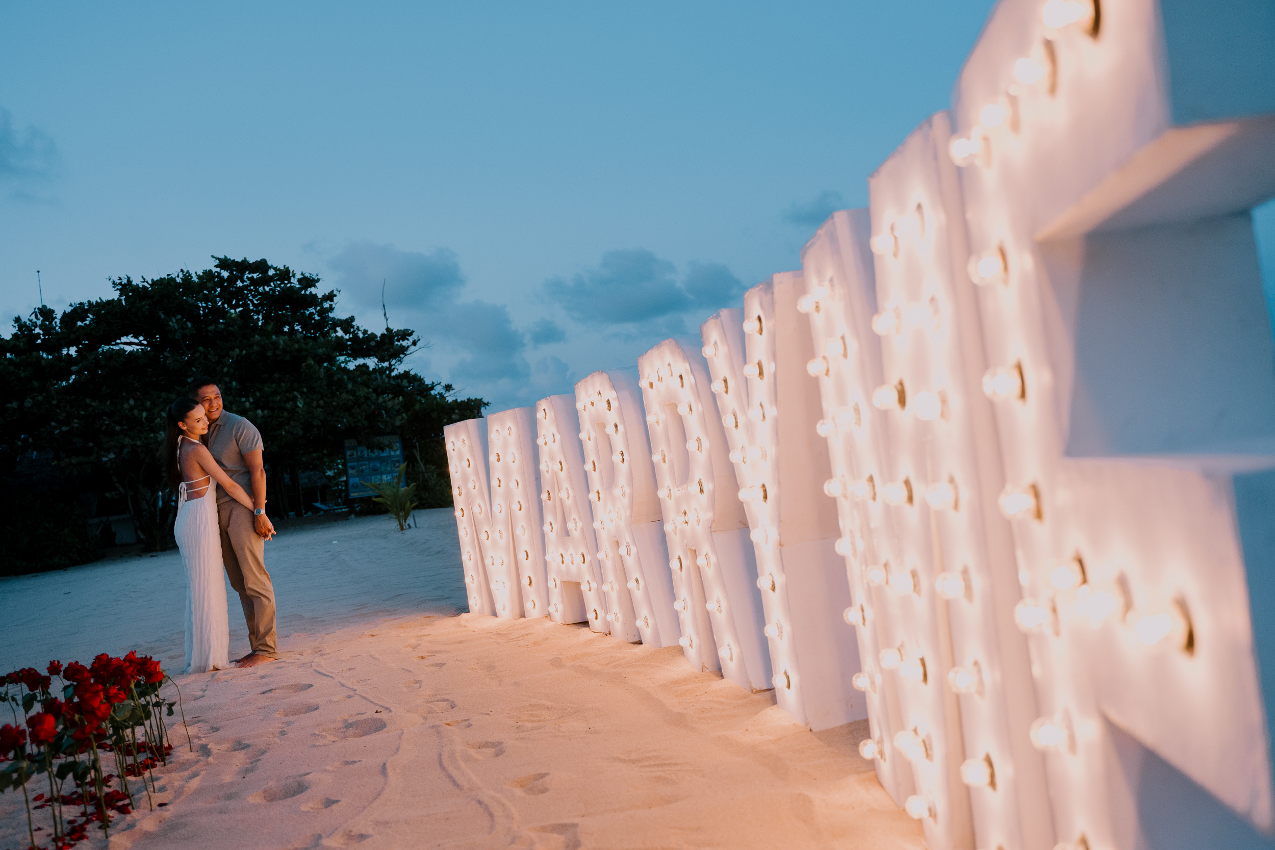 Romantic view of illuminated Marry Me marquee letters along the beach at twilight