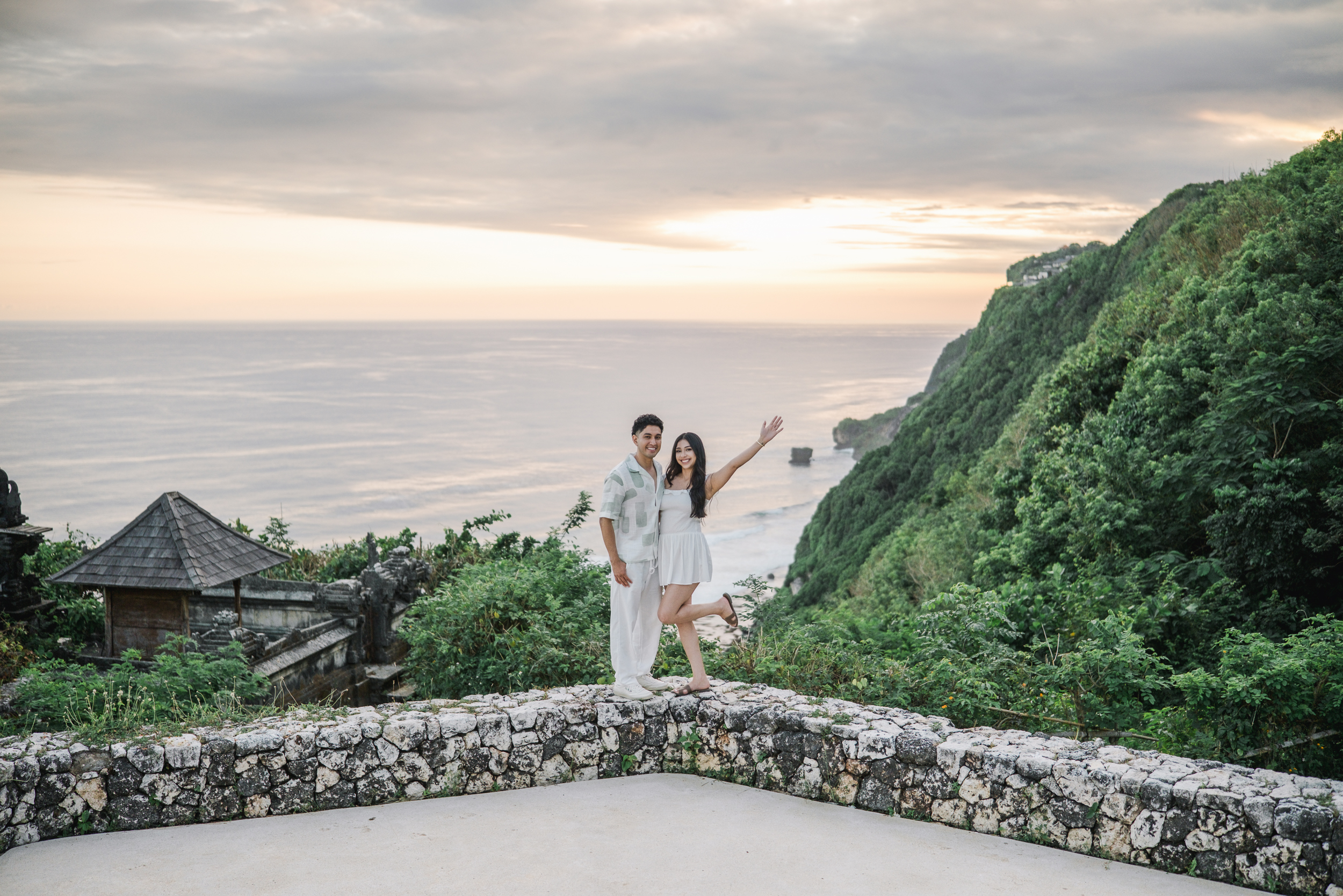 Panoramic sunset view of couple celebrating on an Uluwatu cliff edge