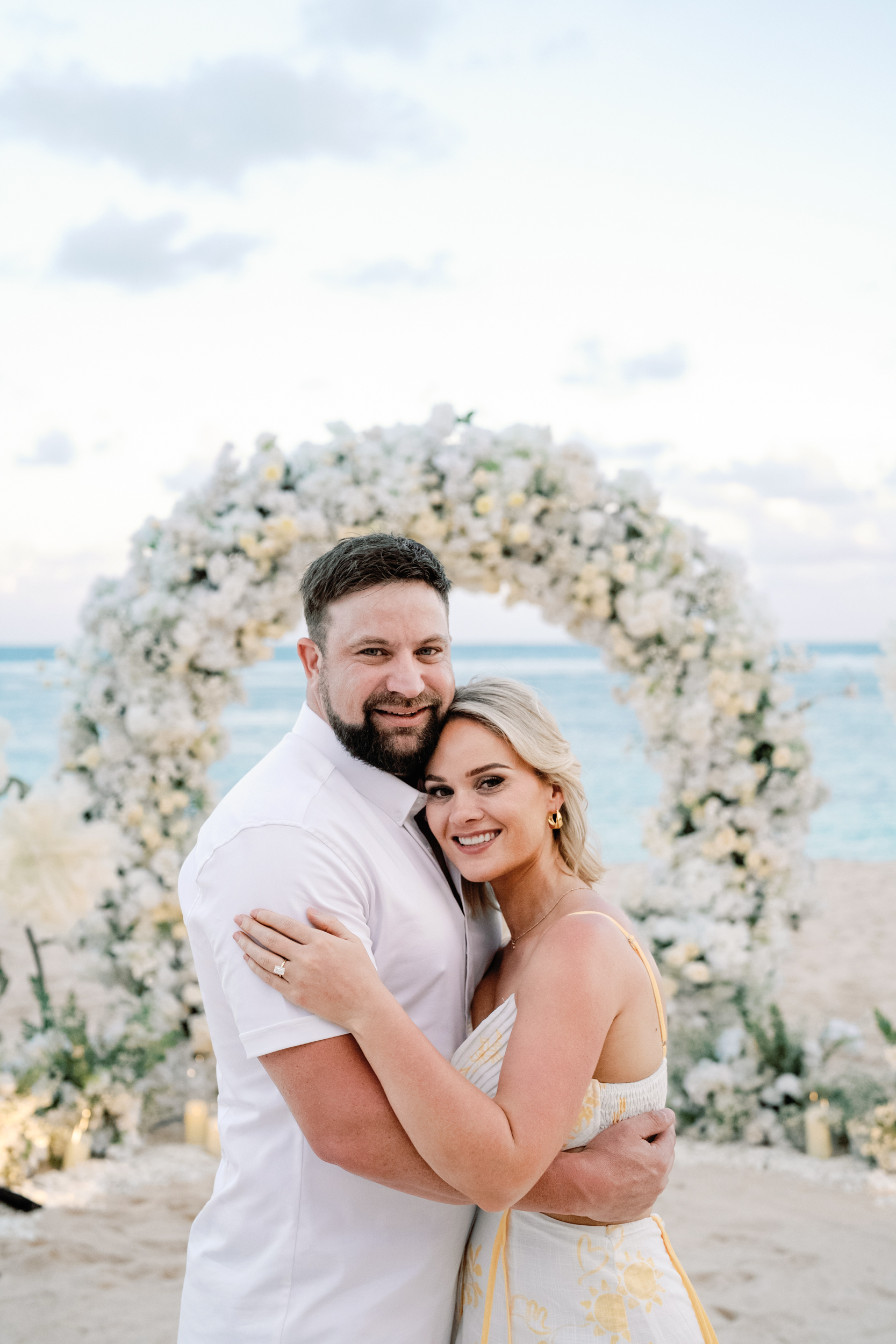 Newly engaged couple smiling after a private beach proposal in Bali with white floral arch.