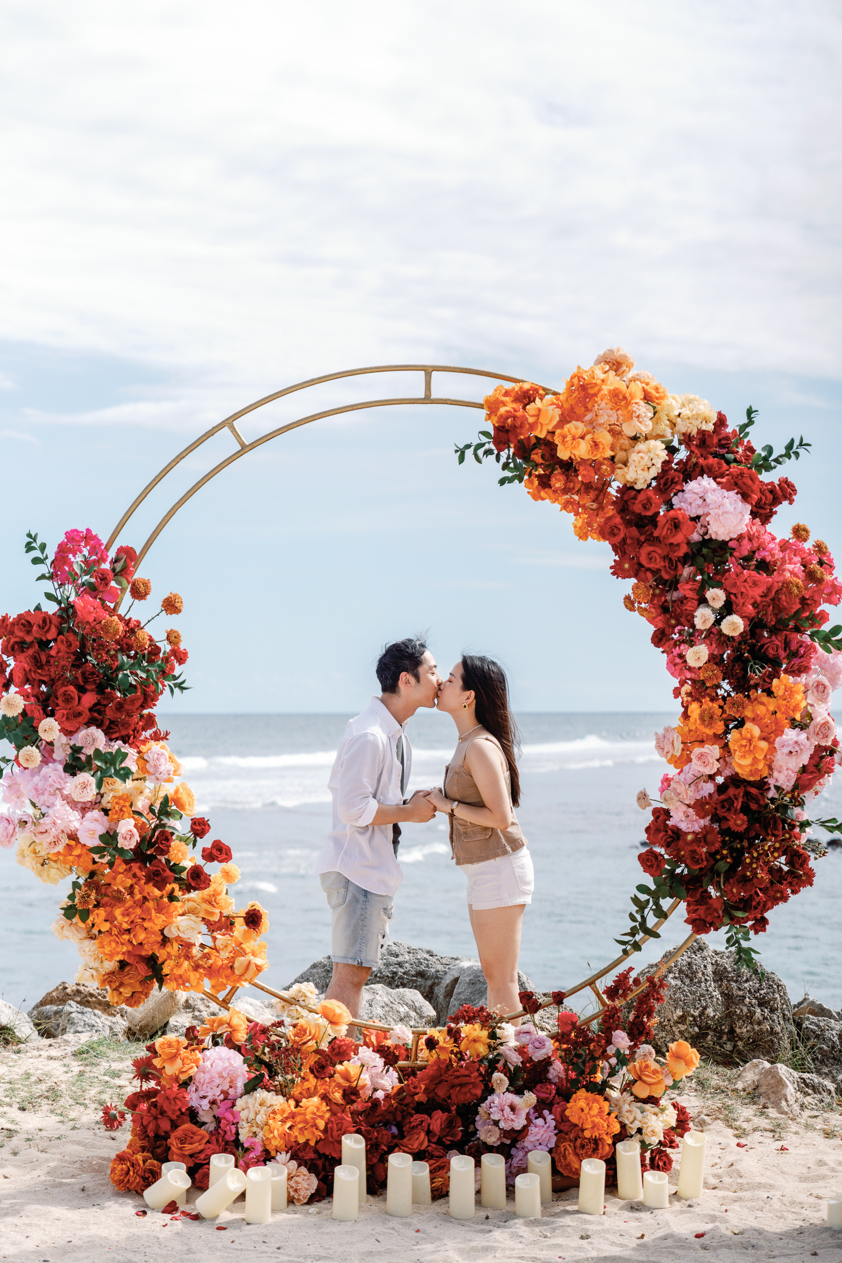 Newly engaged couple embracing inside an orange and red rose floral arch on a Bali beach