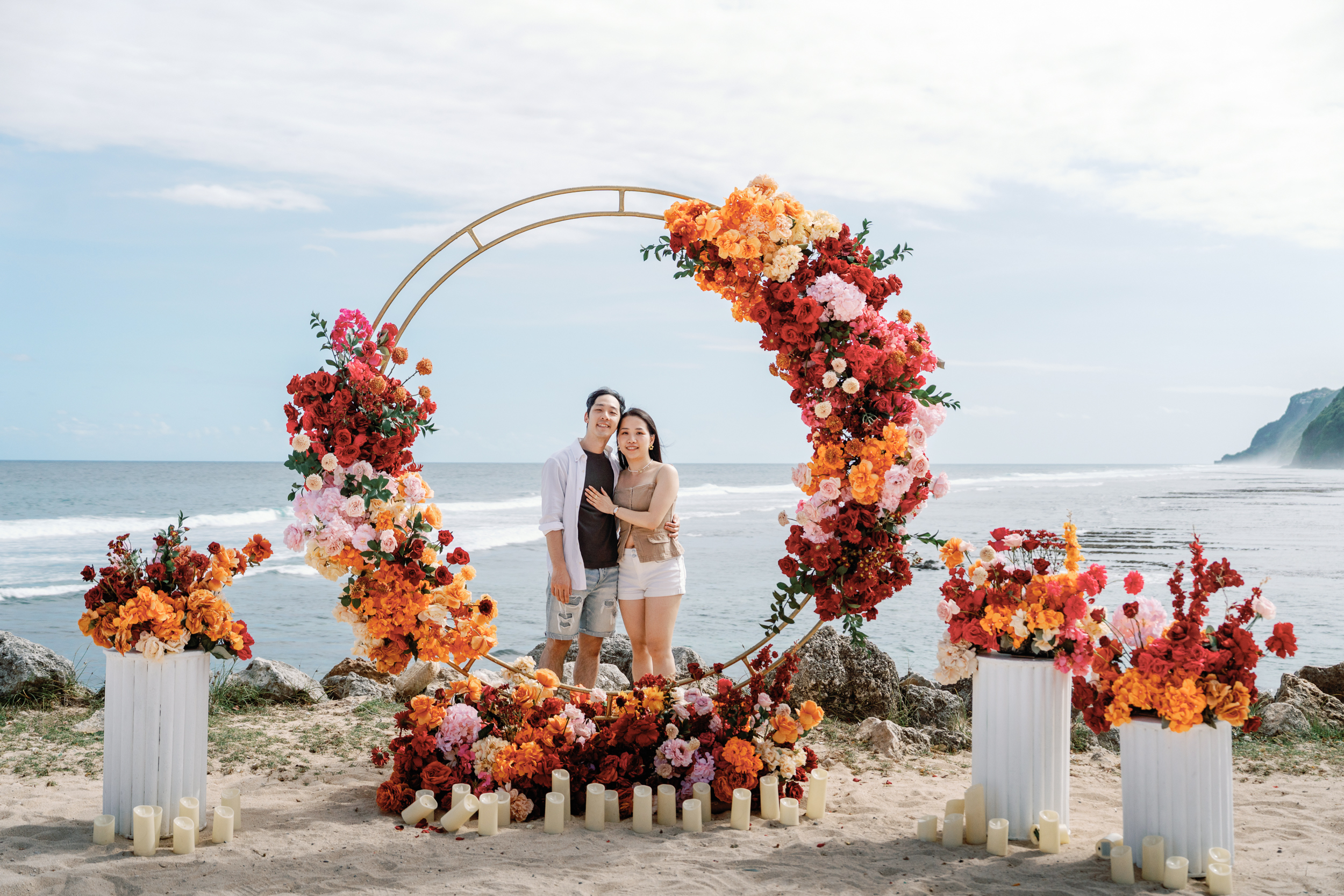 Couple portrait framed by a circular oceanfront floral installation following a Bali proposal