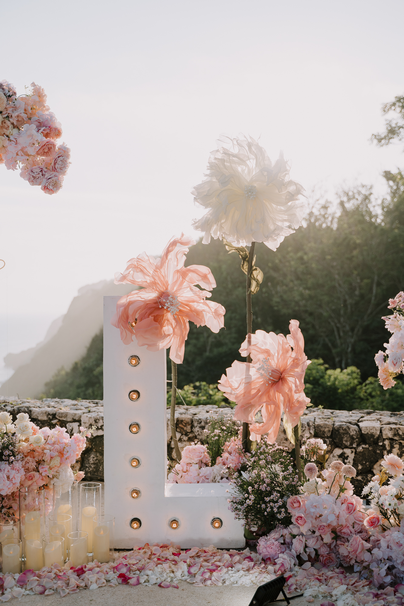 Detail of lit initial marquee letter L and organza floral styling overlooking the Bali coastline