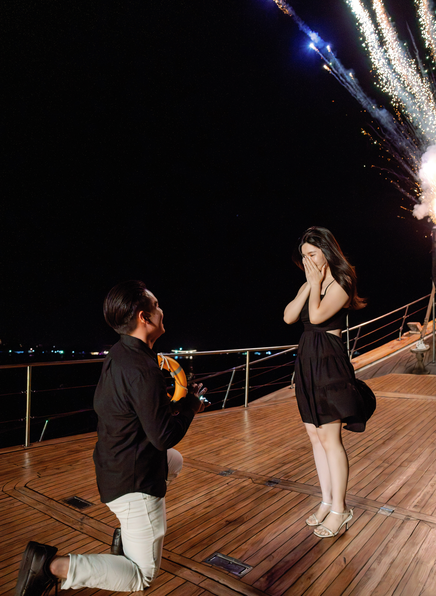 Couple walking towards a cliffside proposal setup with Will You Marry Me written in red rose petals