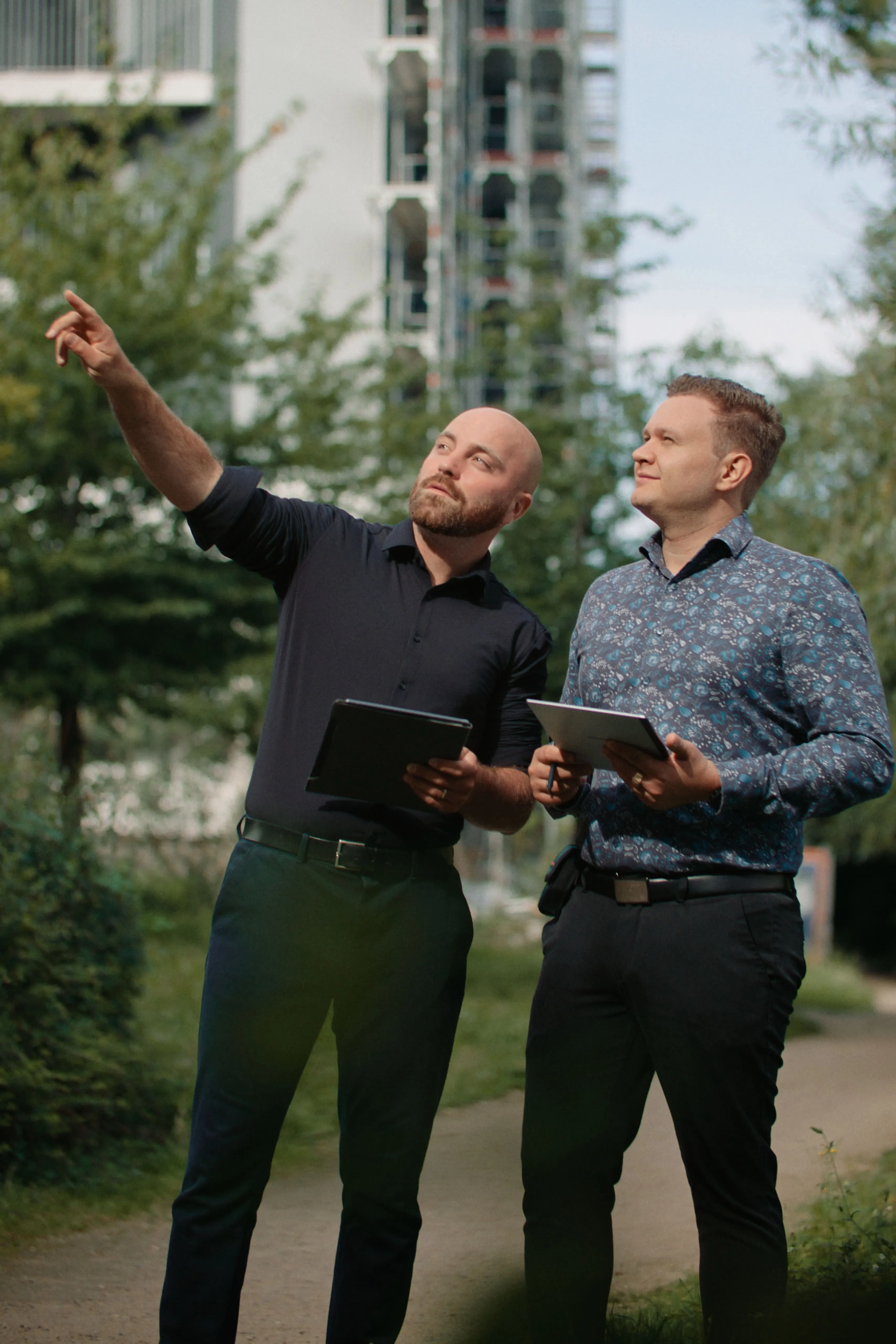 Zwei Energieberater mit Tablets analysieren ein Gebäude im Freien.