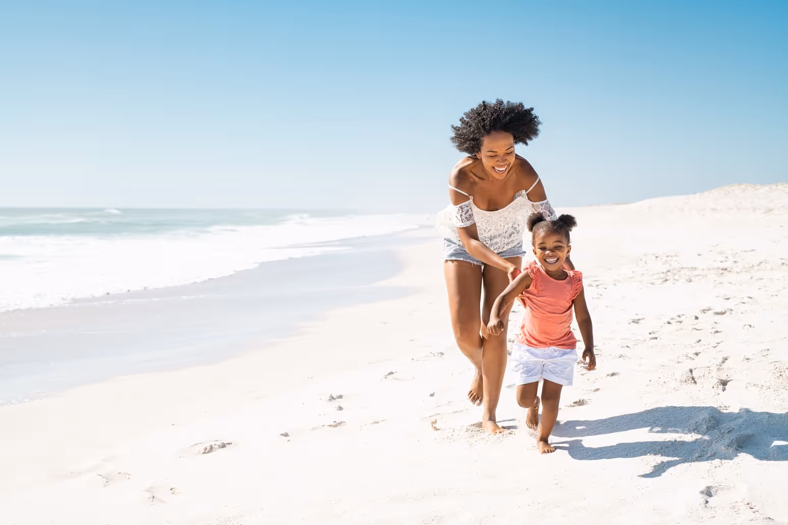 Happy woman and young girl enjoy a fun day outdoors, running hand-in-hand with a nanny, taking in the breathtaking ocean views on a sunny beach together.