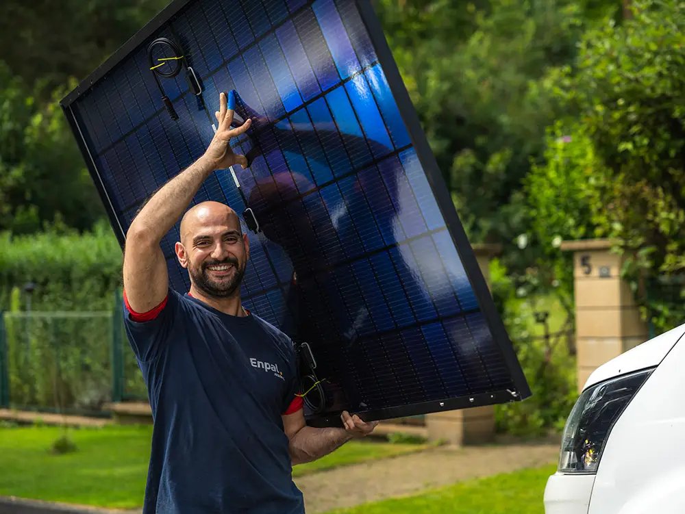 Ein Enpal Handwerker trägt ein Solarmodul und lacht in die Kamera.
