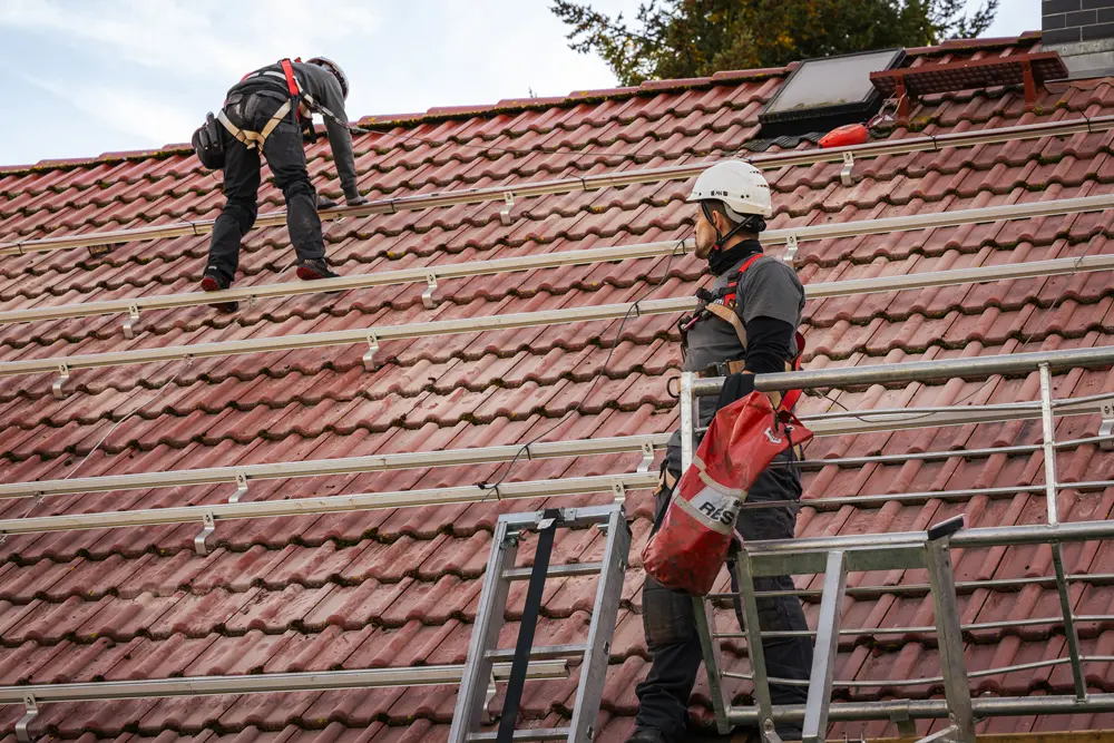 Zwei Solarmonteure auf einem Dach. Auf dem Dach sind bereits Montageschienen angebracht.