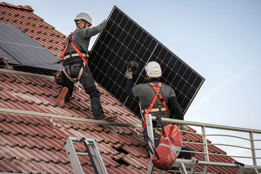 Zwei Monteure installieren ein Solarmodul auf dem Dach.