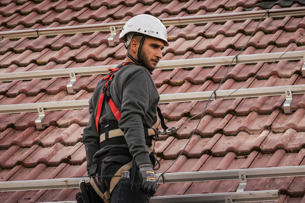 Foto eines Solarmonteurs, der auf dem Dach arbeitet. Es sind vor allem die Schienen und Dachhaken zu erkennen.