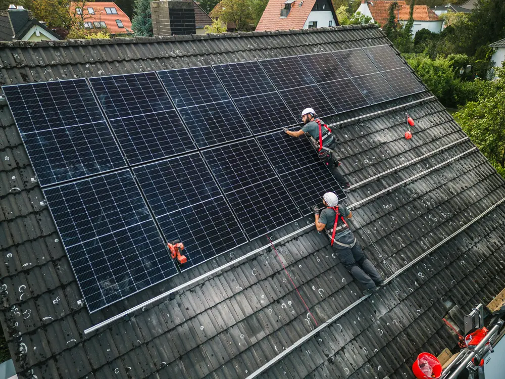 Zwei Monteure auf einem Dach, die Solarpanels installieren.