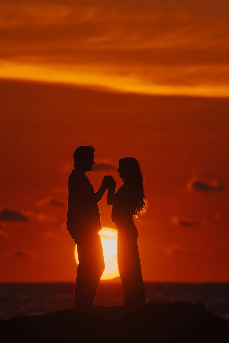 Silhouetted couple holding hands against a fiery orange sunset over the Pacific, showing the golden-hour timing for engagement photos in Costa Rica