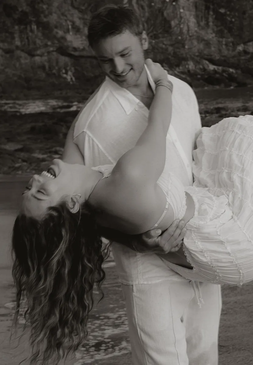 Black-and-white photo of a man dipping his laughing fiancée on the beach in natural, unposed engagement photos in Costa Rica