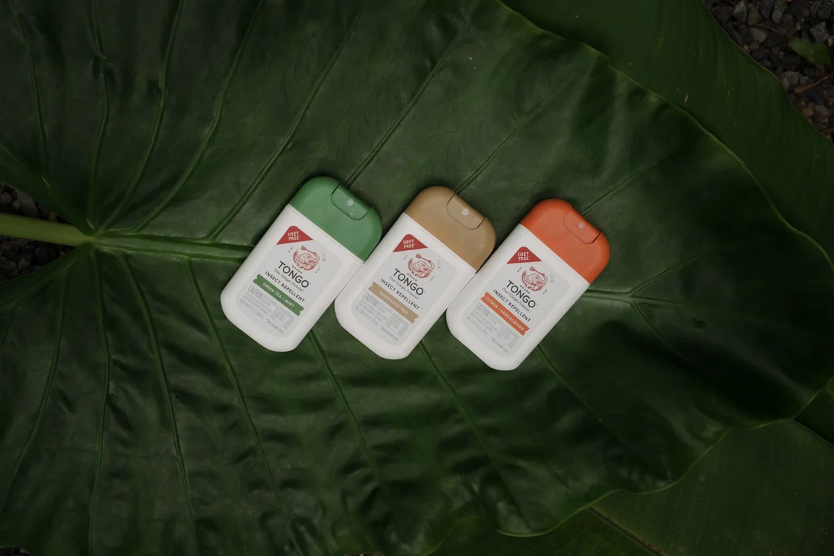 Three travel-size insect repellent bottles laid on a large tropical leaf, product photography in Costa Rica
