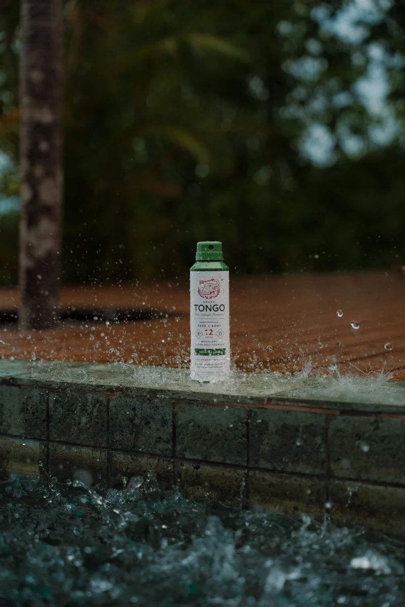 Insect repellent spray bottle on a stone pool edge with water splashing around it, product photography in Costa Rica