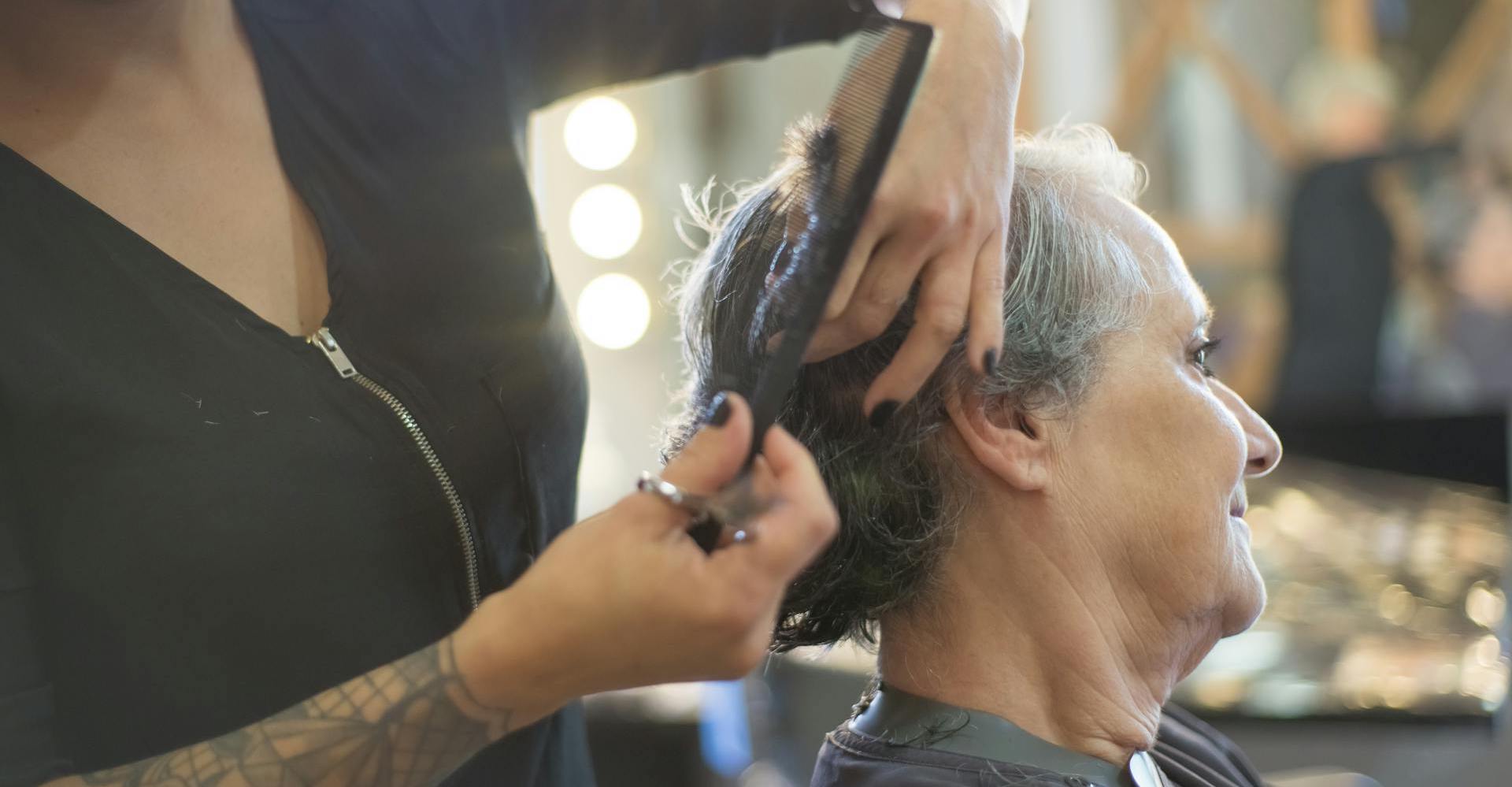 A stylist cuts the hair of a client sitting in a booth.