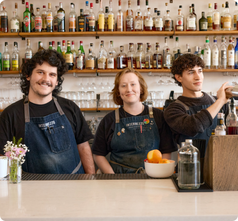 Three restaurant employees standing behind a bar smiling.