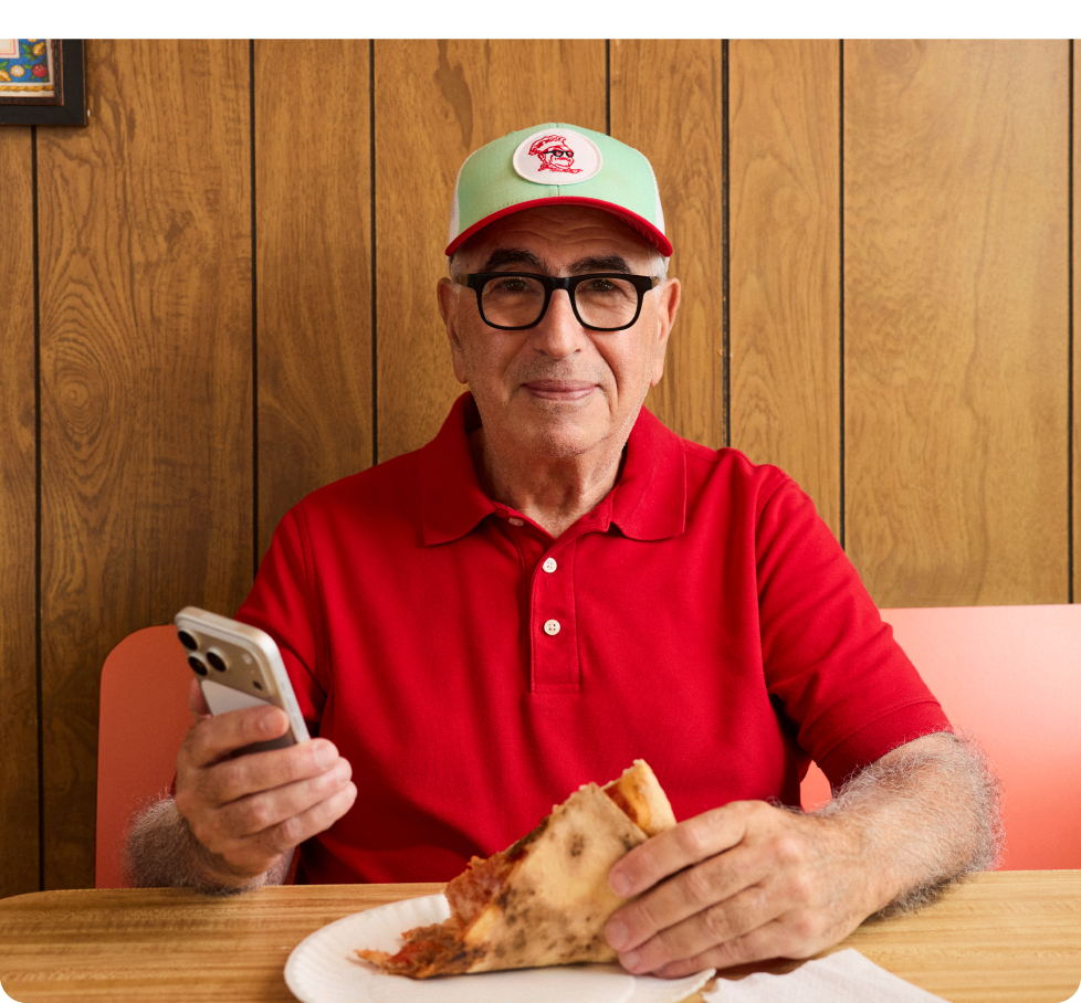 Homebase customer at his restaurant checking the homebase app while eating pizza.