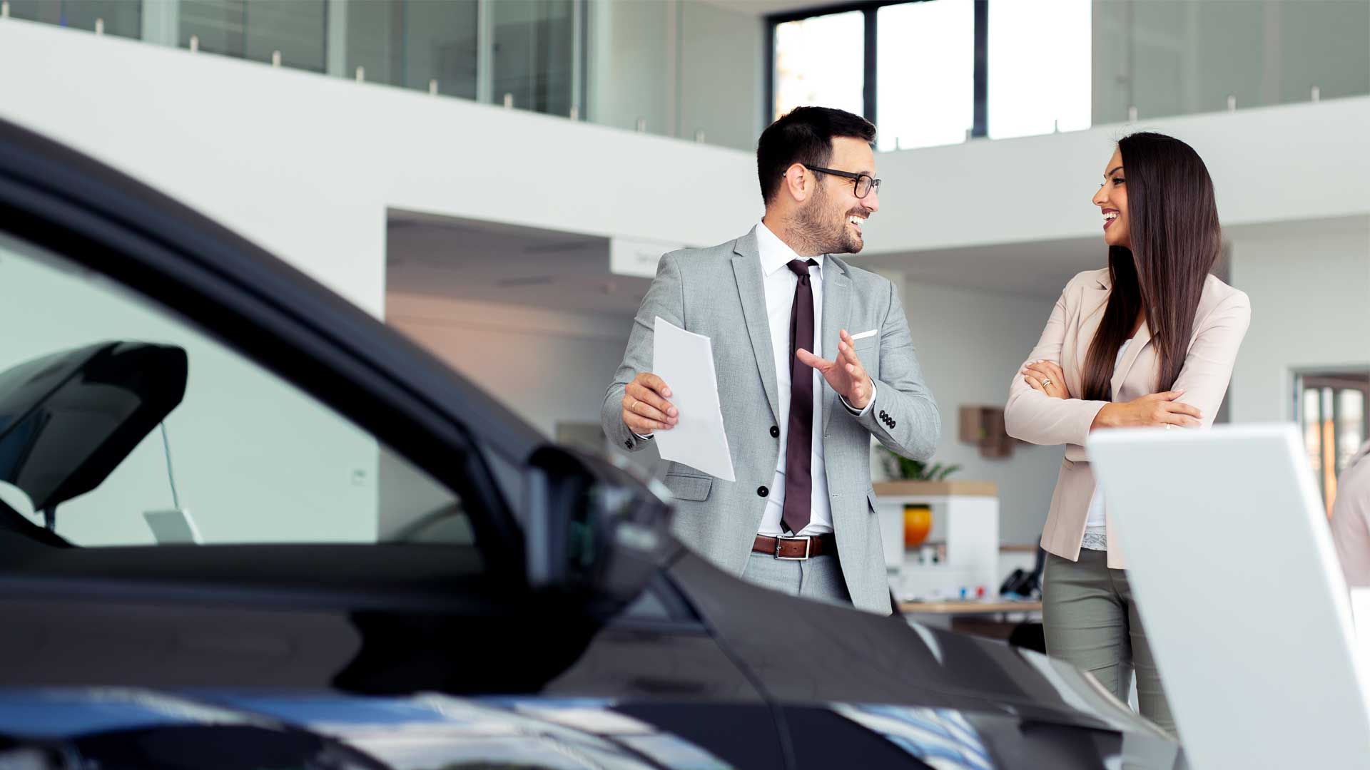 A dealership sales manager reviews a vehicle offer with a customer on the showroom floor.