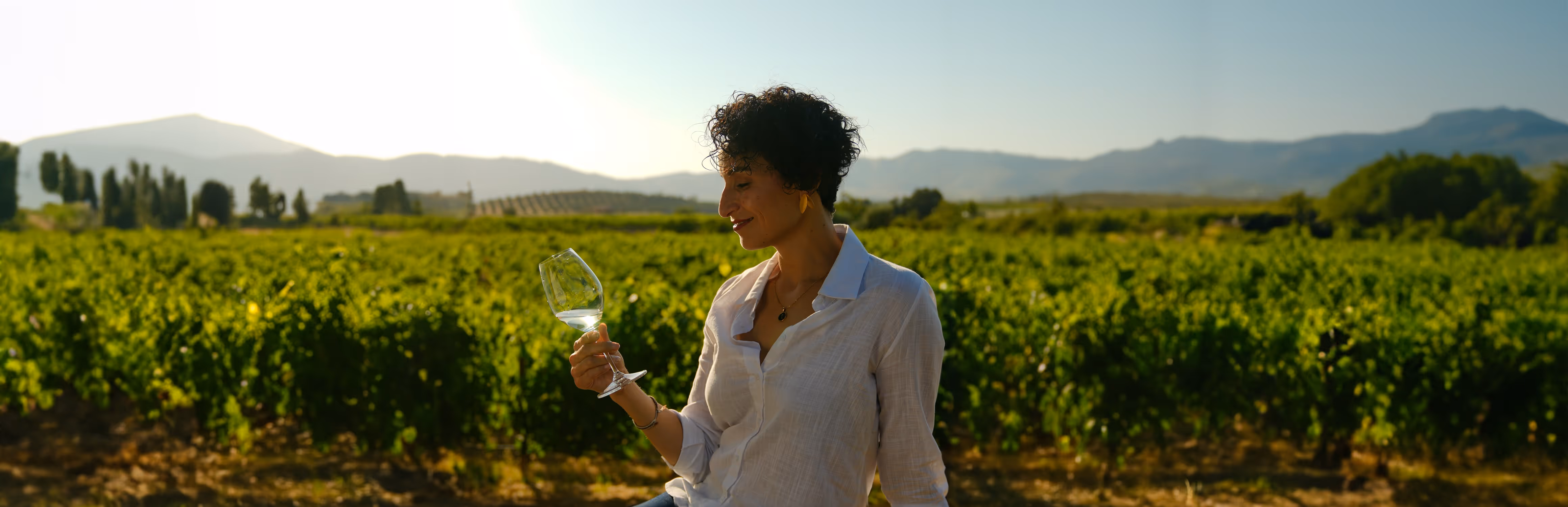 Una mujer tomando vino, con un viñedo de fondo. Baja California