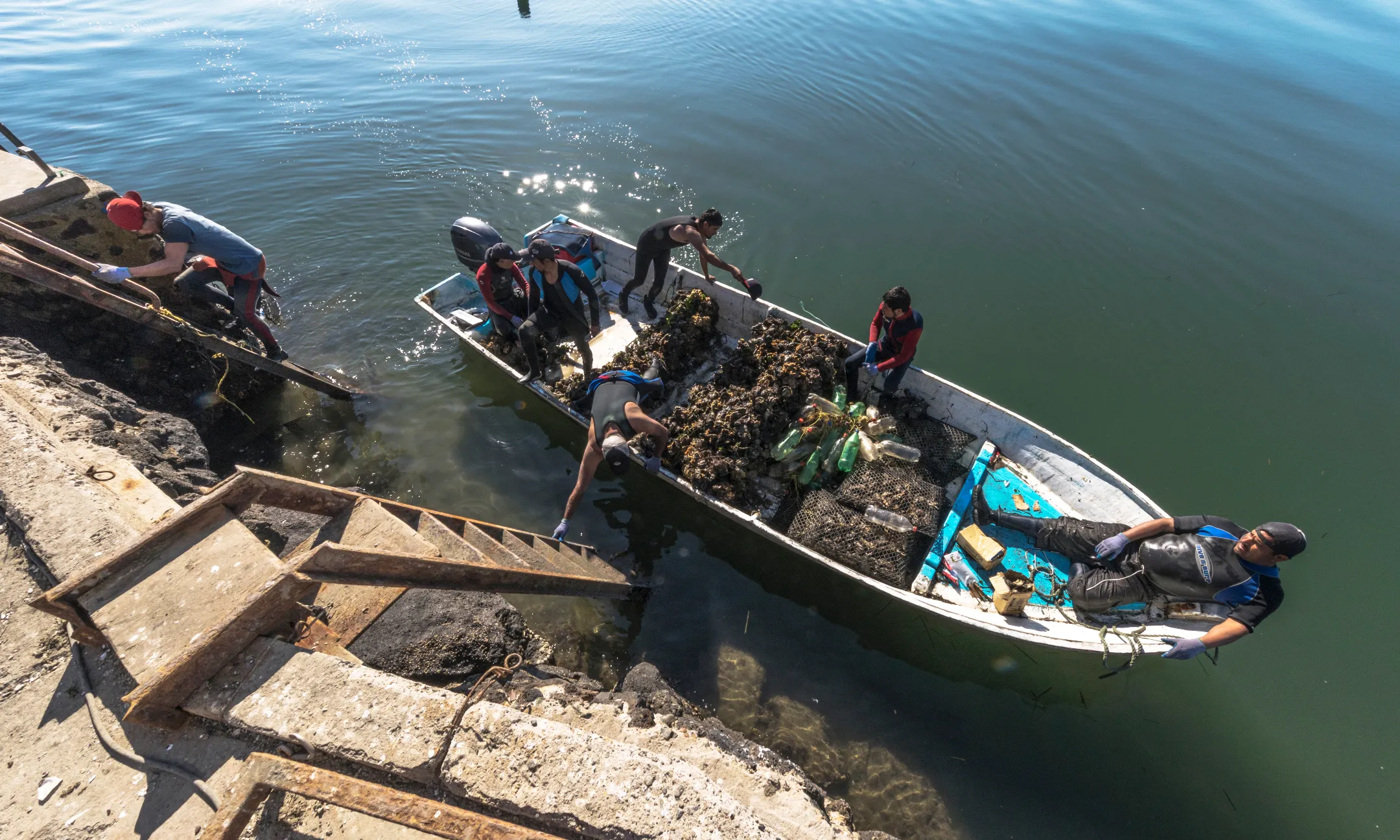 Una chica con sombrero azul y vestido amarillo oliendo flores color lila, sosteniendo vegetales en una canasta. Ruta de las flores